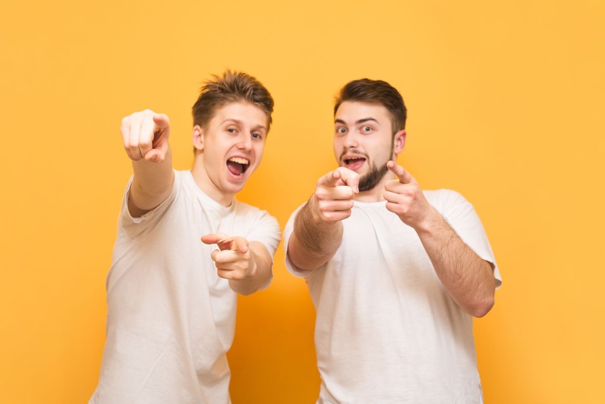 Two happy men in white T-shirts are on a yellow background, looking, smiling and showing a finger in the camera. Two friends are isolated on a yellow background. Copyspace